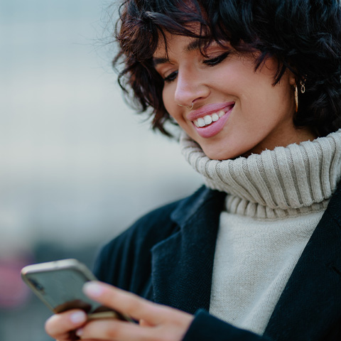 a woman wearing a grey turtleneck holding a mobile phone and smiling