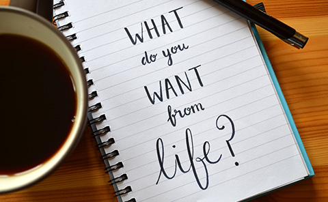 a notepad next to a cup of coffee on a wooden table stating 'What do you want from life?'