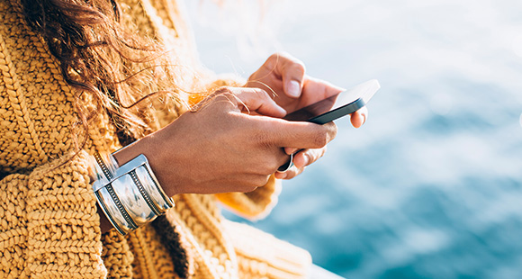 a lady wearing a yellow knitted cardigan and silver bangle texting on a mobile phone