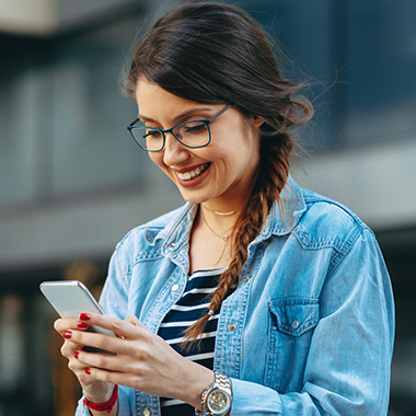 a lady wearing a denim jacket smiling at her phone while texting