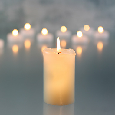 a lit white candle with a number of other candles in the background